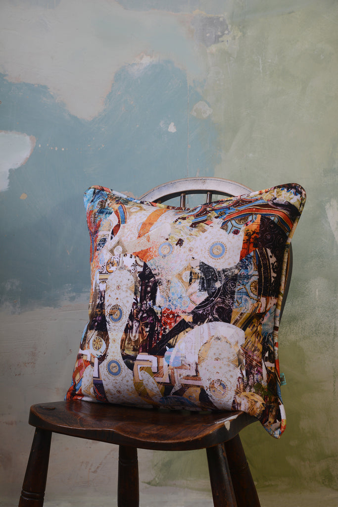 Argo Navis velvet square cushion on a wooden chair against a painted background. 