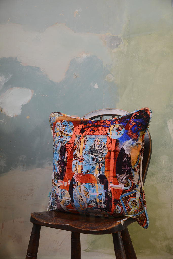 ‘Argo Navis’ velvet cushion featuring blue red and orange abstract patterns sat on wooden chair.