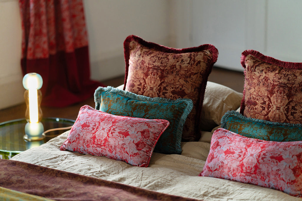 Josephine velvet fringed cushions on linen bedsheets with a Curiousa lamp in the background.