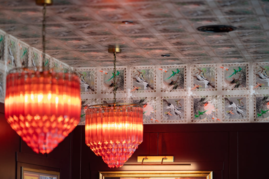 Paradise wallpaper styled as a ceiling mural with ornate chandeliers in a bar setting. 