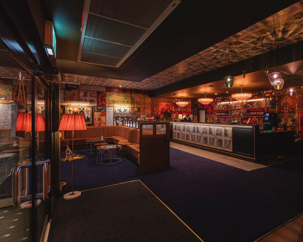 Paradise wallpaper styled as a ceiling mural with ornate chandeliers in a bar setting. 