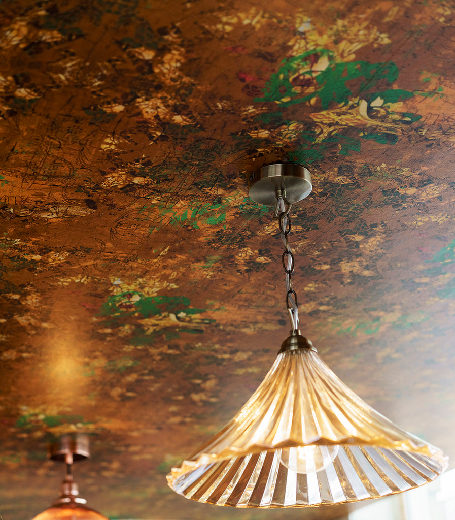 Henry wallpaper in warm golden tones, shown with a chandelier casting light on the design. 
