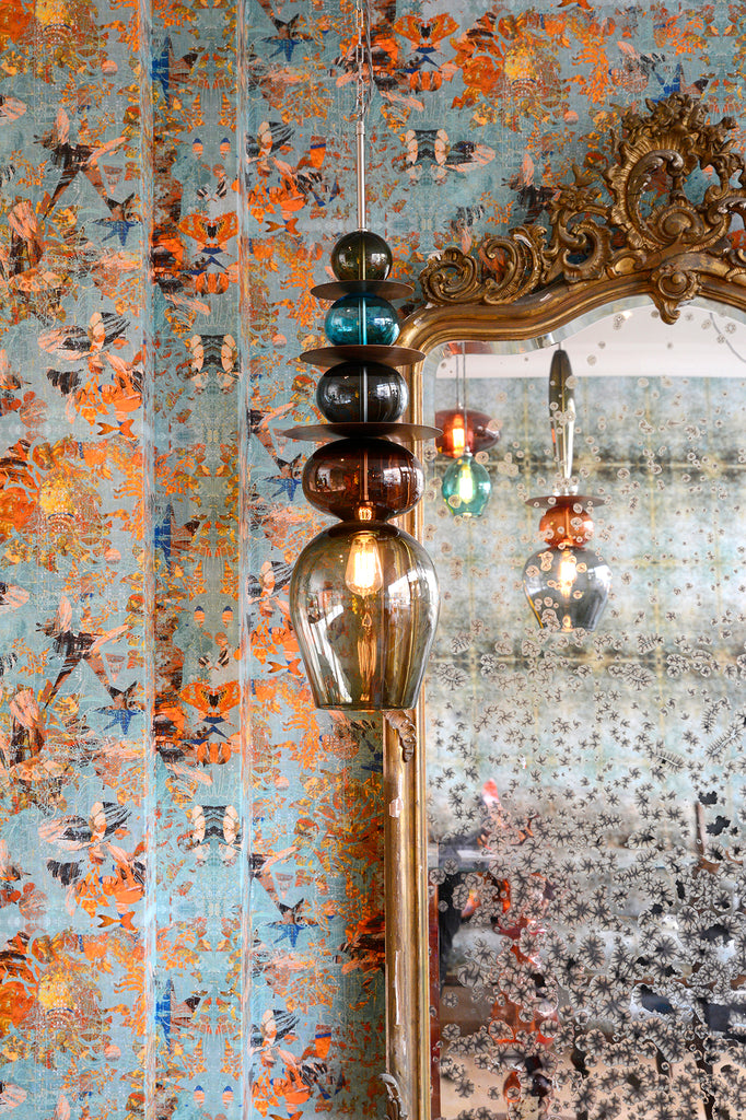 Mary wallpaper featuring abstract geometric designs in orange and teal behind an ornate mirror and a Curiousa glass chandelier. 