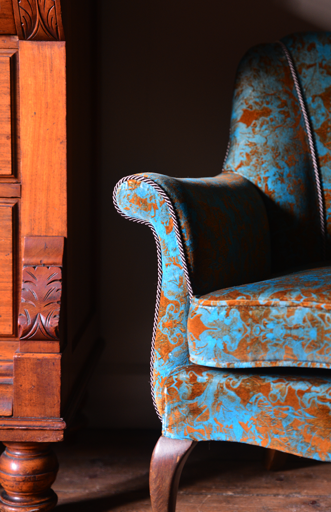 Oscar’ cotton velvet upholstered Blue and orange patterned armchair next to a wooden piece of furniture.