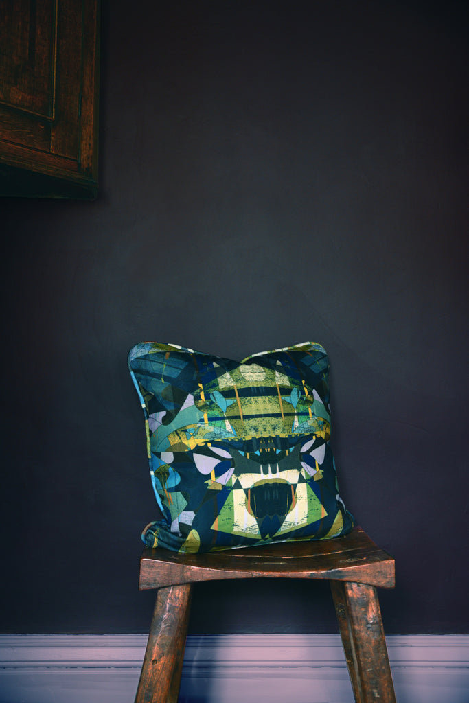 ‘Stevie at the Ritz’ sustainable cushion styled on a wooden stool against a deep blue painted wall. 