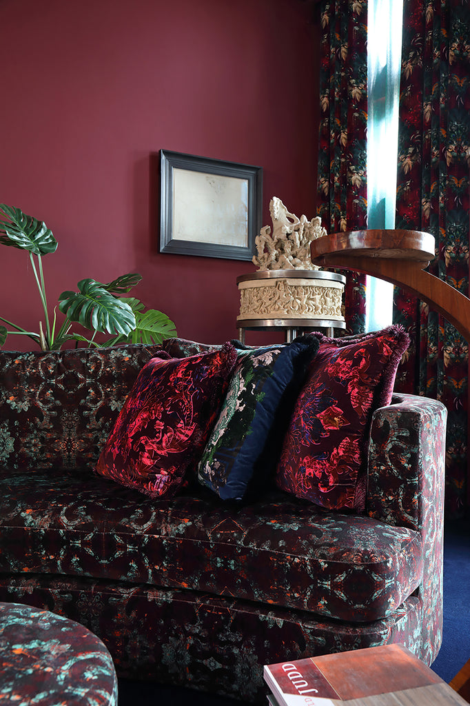 Velvet sofa upholstered in Monk fabric with red patterned cushions in bold interior setting 