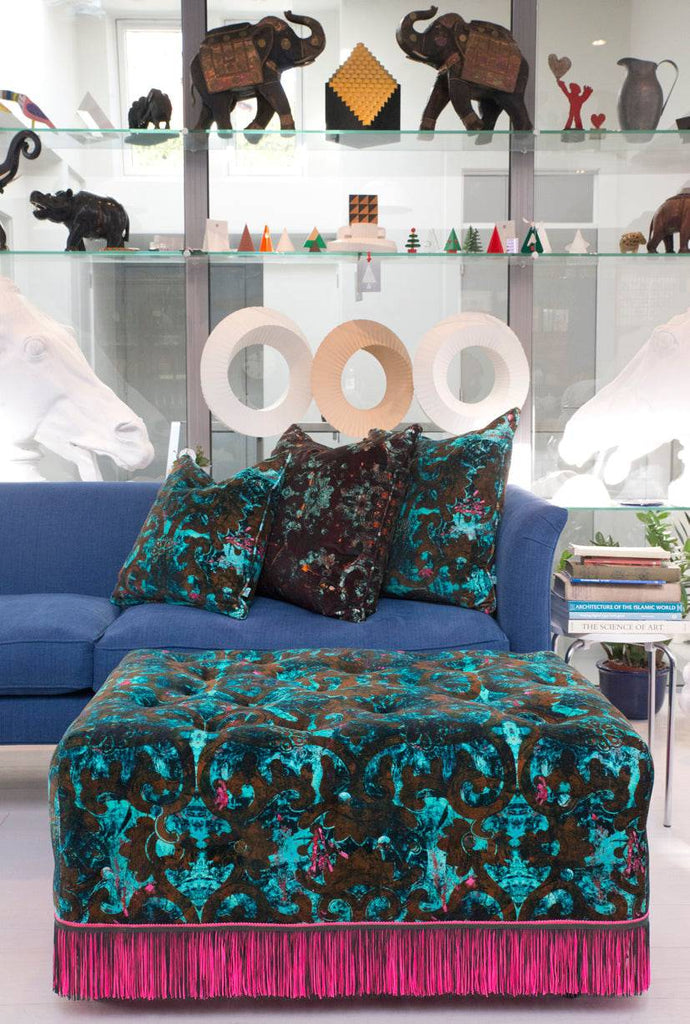 Dizzy velvet upholstered pouffe with pink fringe and matching cushions on blue sofa with Dizzy velvet cushions 