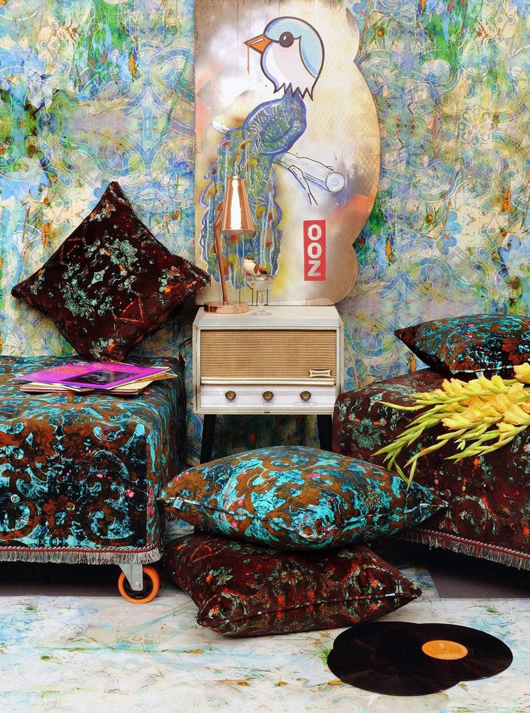 Birdland wallpaper behind an electric mix of art, cushions, and velvet pouffe chairs in jewel tones.