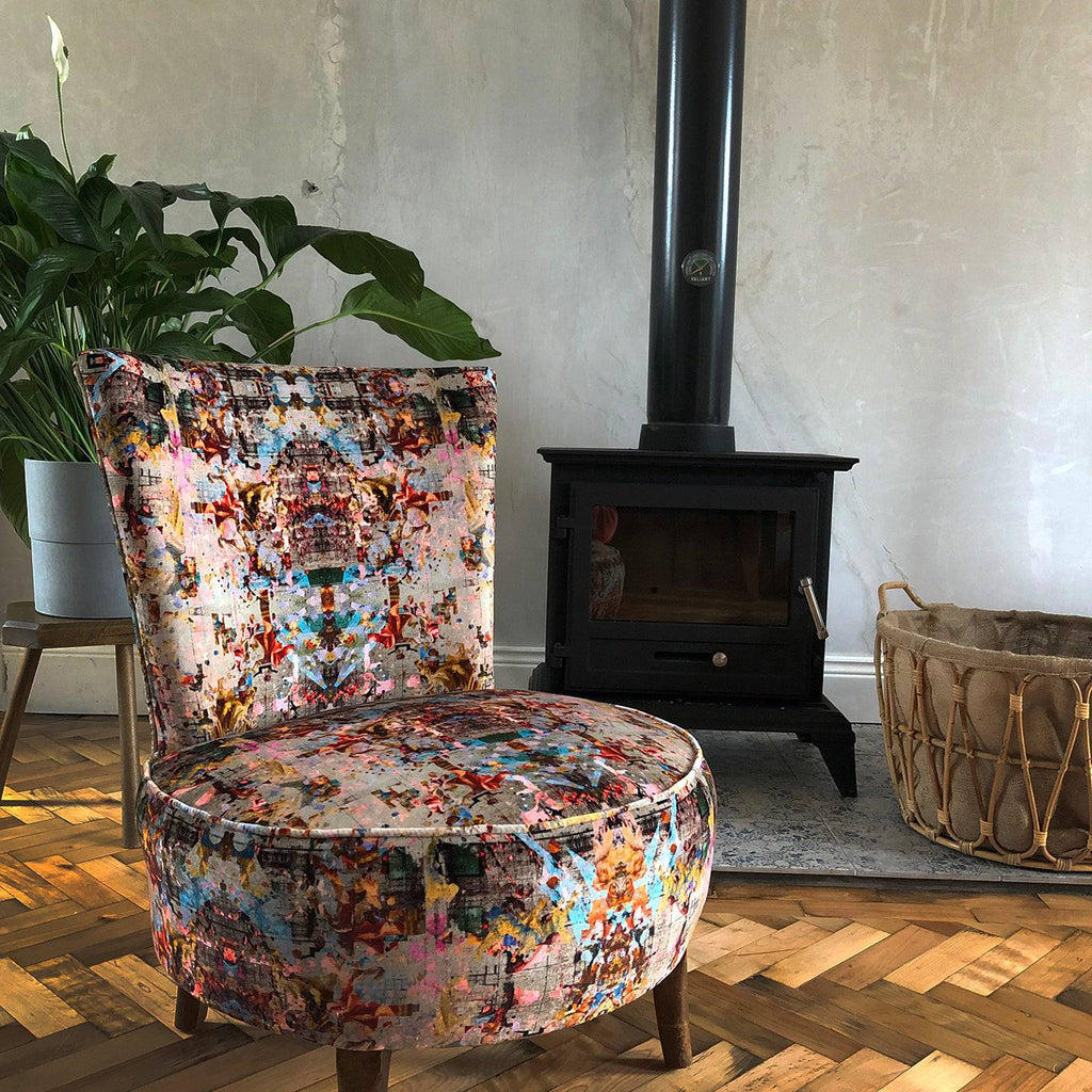 Vintage-style armless chair upholstered in Neo13 designer velvet with multicoloured architectual print in red, pink, teal and ochre, styled in a room 