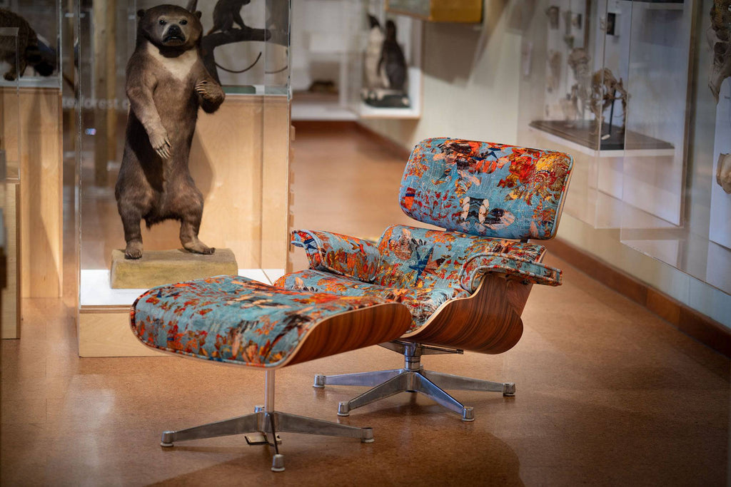 Eames-style chair upholstered in ‘Mary’ luxury cotton velvet, featured blue and orange geometric patterns styled in a museum interior. 